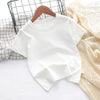 A white classic cotton crew neck t-shirt for kids is displayed on a white surface next to a mesh basket and a beige knitted f