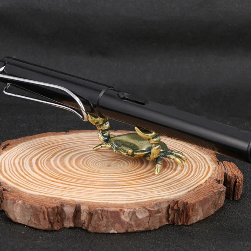 A brass crab figurine is placed on a wooden slice next to a black desk tool.