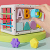 A hand is sorting colorful letter shapes A through D using an educational cube with elastic bands.