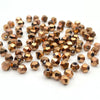 A pile of small, faceted bicone crystal glass beads in a gold tone for jewelry making.