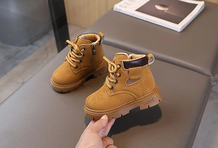 A pair of tan kids' winter leather boots with laces and a side zipper resting on a gray surface.