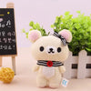 A fluffy white Rilakkuma anime plush bear standing in front of a potted green plant and a chalkboard sign.