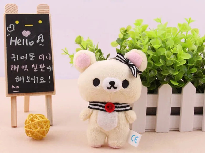 A fluffy white Rilakkuma anime plush bear standing in front of a potted green plant and a chalkboard sign.