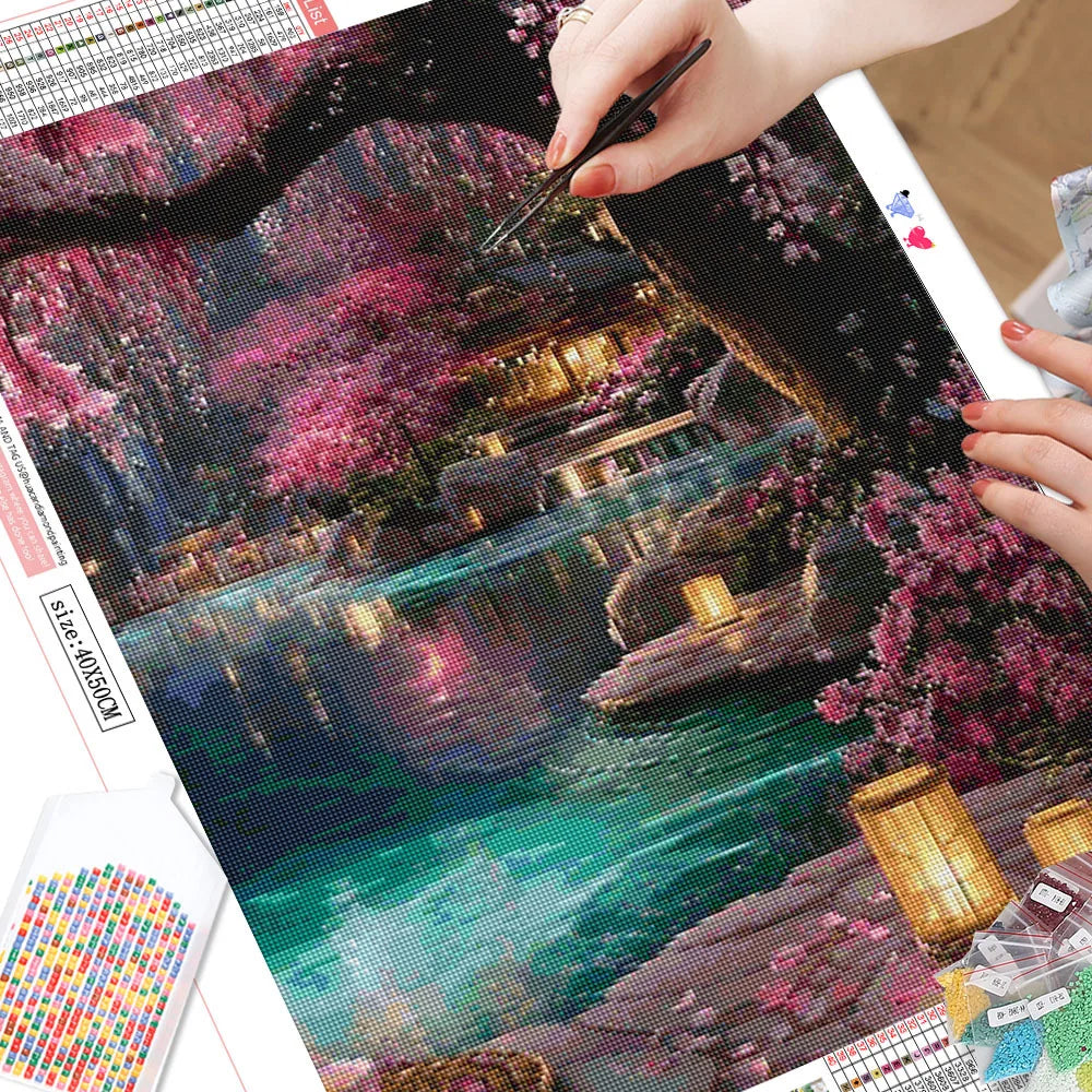 A close-up of a diamond painting kit featuring a vibrant pink and green landscape with a flowing river and traditional archit