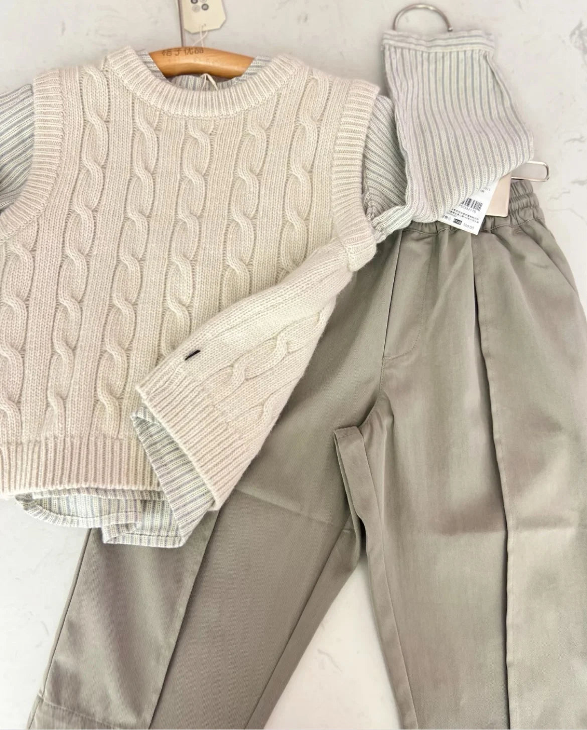 A beige knit sweater and matching trousers set for a child, displayed on a light background.