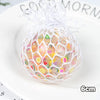 A spherical stress relief ball made of mesh netting filled with colorful, translucent materials on a white plate.