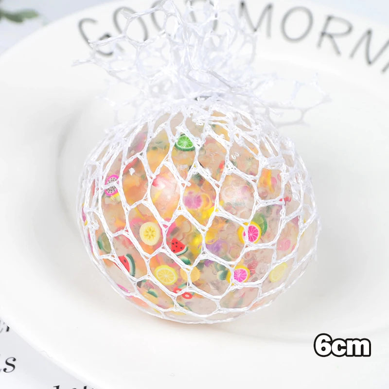 A spherical stress relief ball made of mesh netting filled with colorful, translucent materials on a white plate.