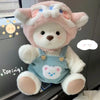 A pink teddy bear plush toy wearing a light blue overalls and a white collar.