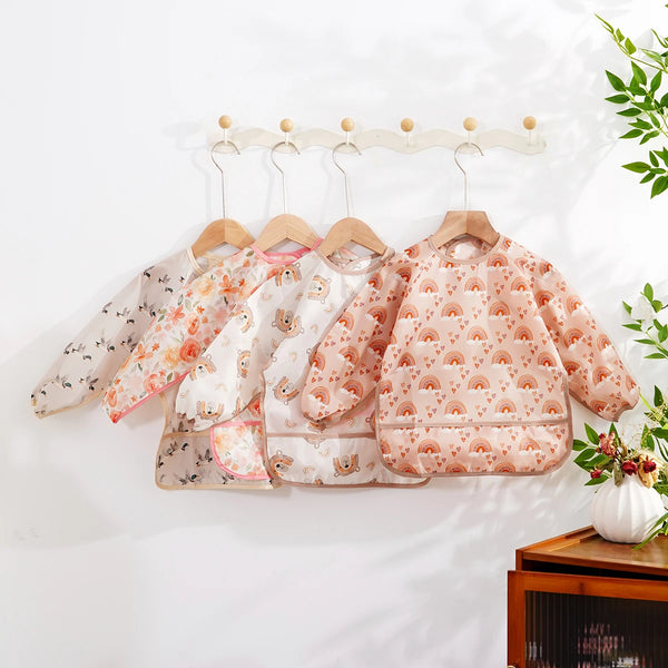 Eine Ansammlung süßer wasserfester Baby-Babyschüren mit langen Ärmeln an einem Holzregal.