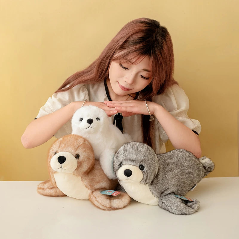 Three realistic seal plush toys in white, brown, and gray are displayed on a white surface.
