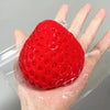A bright red squishy strawberry fidget toy is held in a person's hand, packaged in clear plastic.