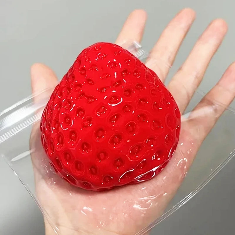 A bright red squishy strawberry fidget toy is held in a person's hand, packaged in clear plastic.