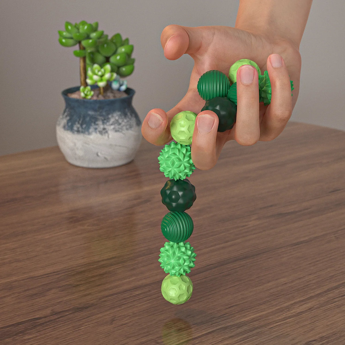 A hand holds a string of soft green silicone massage balls with magnetic cores against a blurred background.