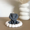 A gray silicone mold shaped like an elephant sits in a white ring on a brown surface next to a white vase.