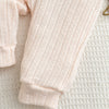 A light pink knitted baby romper and pants set laid flat on a white textured fabric.