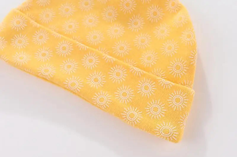 A yellow knitted baby hat with a repeating white daisy pattern.