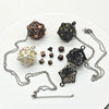 A set of metal polyhedral dice with pendant storage cases displayed on a white background.