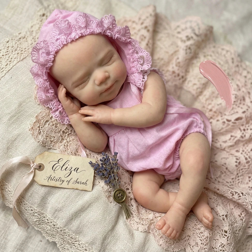 A newborn silicone reborn baby doll with pink lace bonnet lying on a pink crocheted fabric.