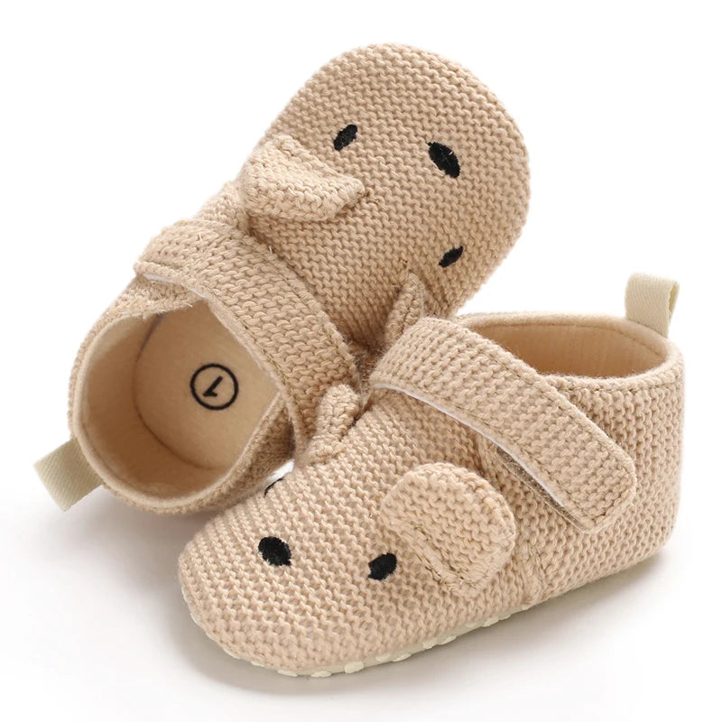 A pair of beige soft cotton baby walking shoes with a duck face design.