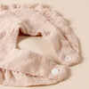 A light pink cotton ruffle baby bib is shown flat on a beige background.