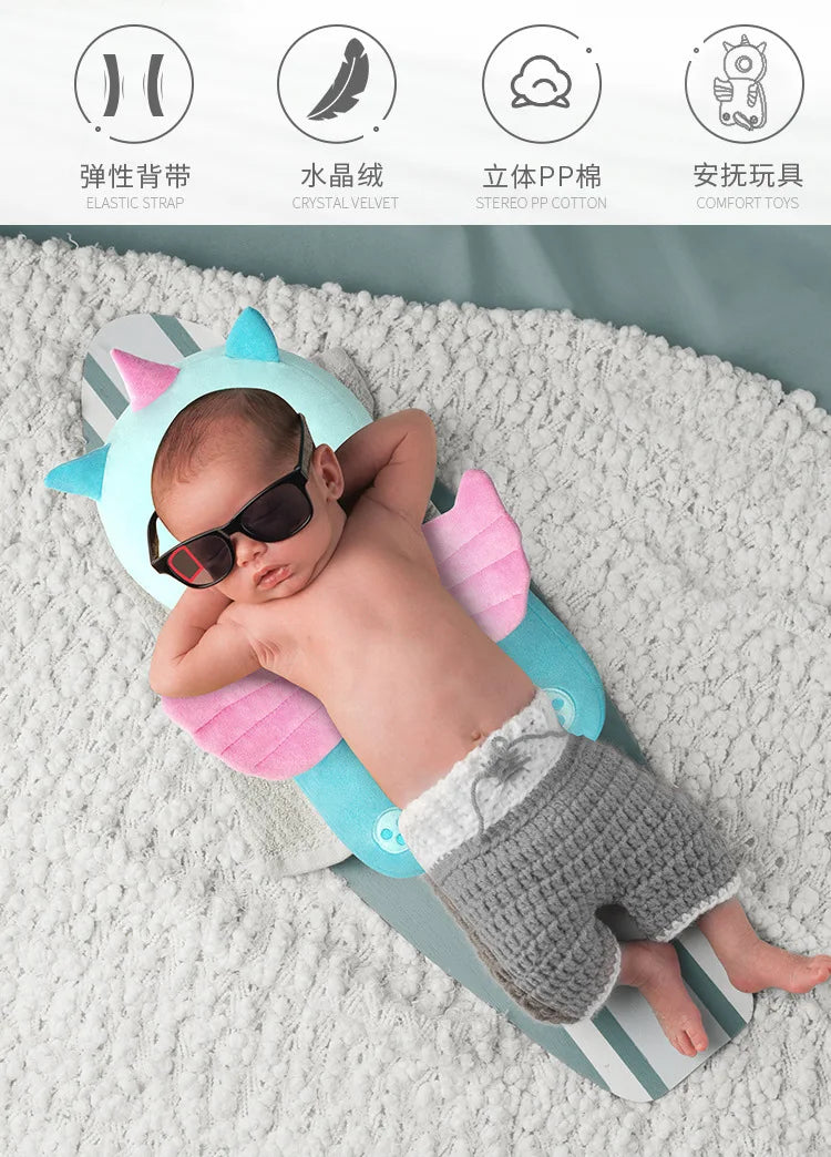 A newborn baby is lying on a soft, light-colored surface inside a blue and pink security pillow backpack.