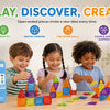 A child plays with colorful magnetic tiles on a wooden table, surrounded by various building structures.