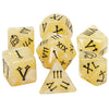 A set of seven elegant polyhedral dice in a pale yellow color, showing various Roman numerals and symbols.