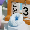 A light blue, squishy stress relief ball is displayed in front of a wooden frame with numbered tags.