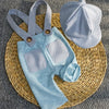 A light blue knit romper and matching newsboy cap set resting on a woven mat.