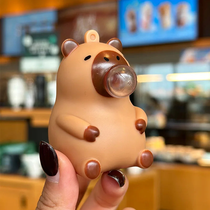 A hand holds a small, light brown capybara squeeze toy with a clear bubble blowing feature.