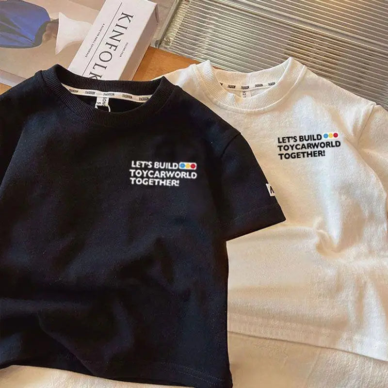 A black crew neck t-shirt with the text LET'S BUILD TOYCARWORLD TOGETHER on the chest, next to a white t-shirt.