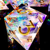 A handcrafted resin polyhedral die set with light purple and gold numbers resting on a dark surface.