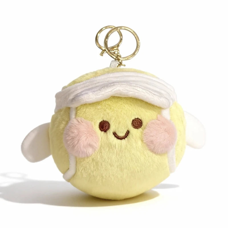 A yellow plush ball with a white bandage wrap and pink pom-poms, attached to a gold-colored keychain.