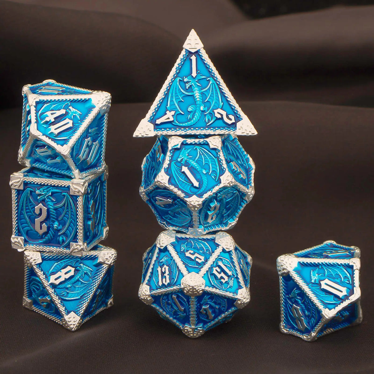 A set of seven blue and silver metal polyhedral dice, including a pyramid shape, displayed on a dark surface.