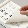 A hand is holding an open line art drawing book showing various simple anime character eyes and facial outlines for tracing.