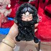 A hand holds a black Skullpanda You Found Me! Series collectible figure with dark hair and closed eyes against a red fuzzy ba