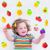 A smiling toddler holds various colorful fruit and vegetable squishy toys above her head.
