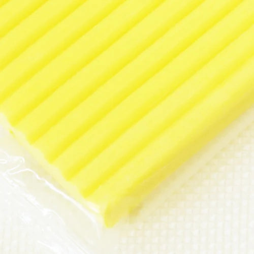 A close-up of a bright yellow, ridged polymer clay block resting on a white surface.