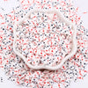 A pile of pink and white polymer clay sprinkles mix scattered on a white surface.