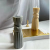 A tall, twisted ribbed silicone candle mold in gray and cream colors sits on a gold base.