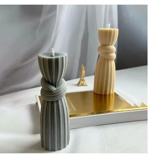 A tall, twisted ribbed silicone candle mold in gray and cream colors sits on a gold base.