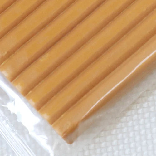 A close-up view of a rectangular block of soft, yellowish-orange polymer clay modeling material.