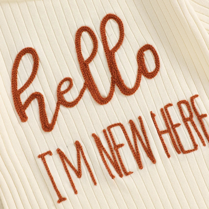 A close-up of a cream ribbed garment featuring hand-stitched brown text that reads Hello I'm new here