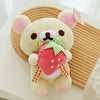 A cute plush toy of a bear with pink ears holding a strawberry shaped accessory.