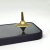 A brass metal fidget spinner with a smooth, tapered top resting on a dark rectangular surface.