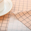 A light pink checkered fabric is laid on a table next to a white cup and saucer.