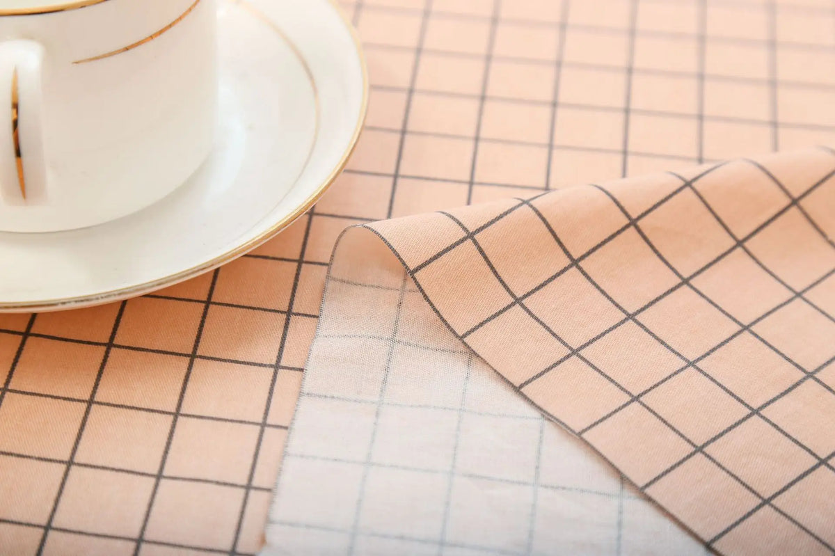 A light pink checkered fabric is laid on a table next to a white cup and saucer.