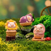 A collection of three cute pig figurines in various colors and textures set in a mossy garden landscape.