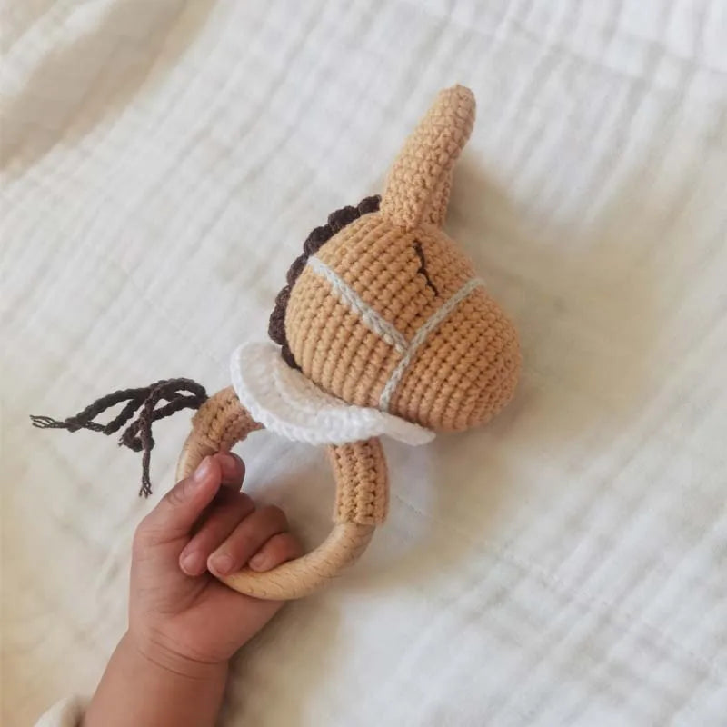 A hand is holding a wooden baby rattle and teether ring shaped like an otter.