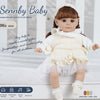 A lifelike 14-inch reborn baby doll with a white outfit and bonnet is shown in a studio setting.